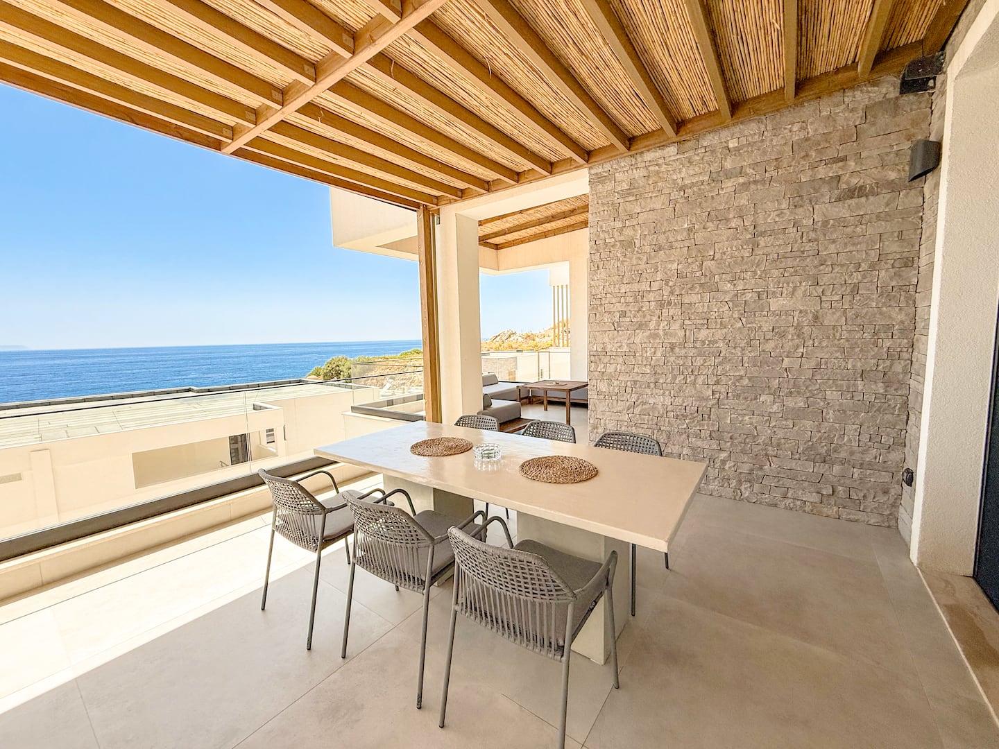 Shaded veranda dining at Villa 4 — long table, sea view through the timber pergola.